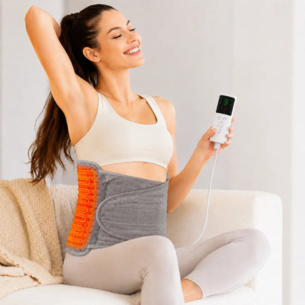 Woman wearing LULIQUA heated back belt for lower back pain relief, sitting comfortably on a sofa holding the digital controller